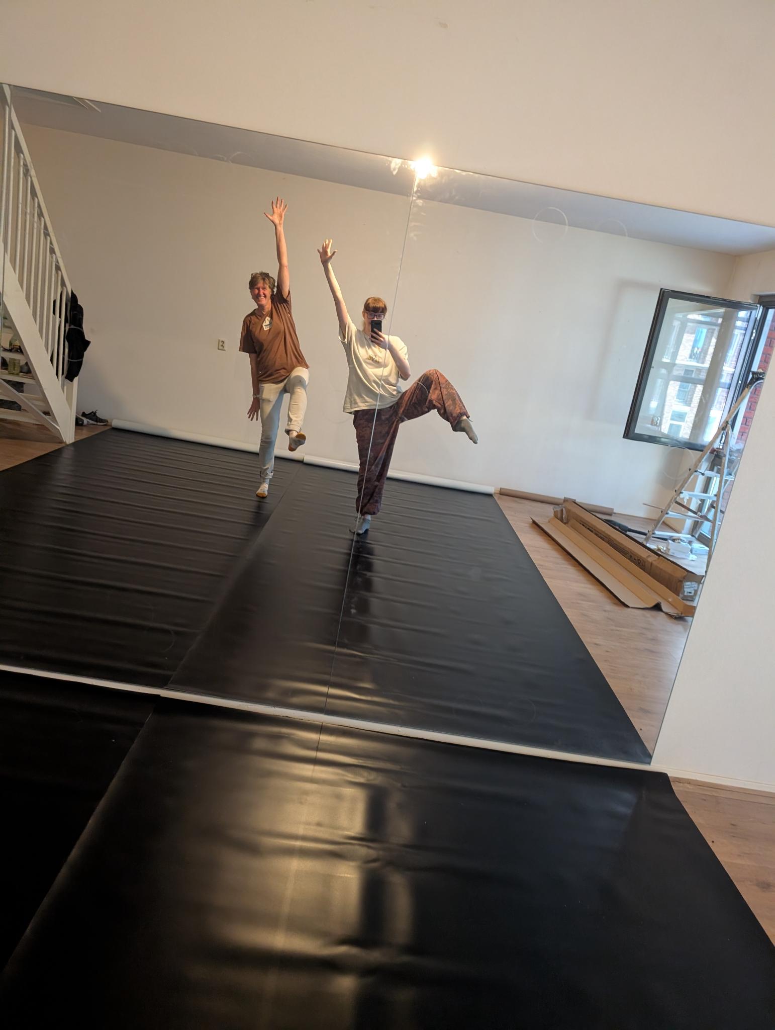 Two dancers mid-pose, arms raised, in the freshly-floored TUMACH studio